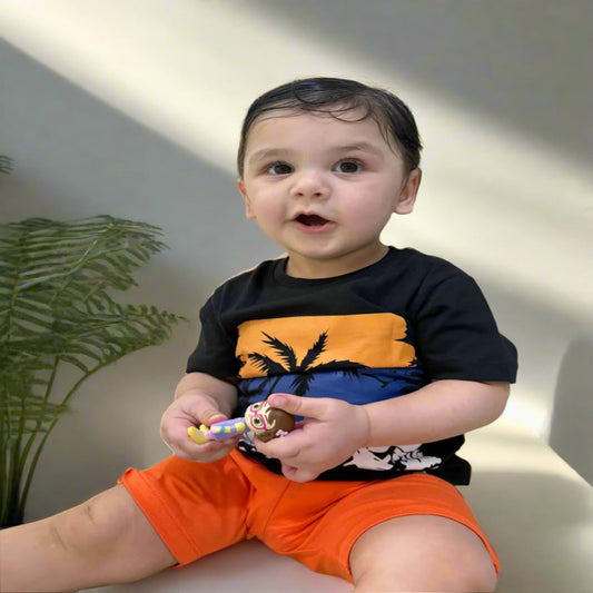 Child wearing a black, orange, and blue shirt with a toy in hand against a light-colored wall.
