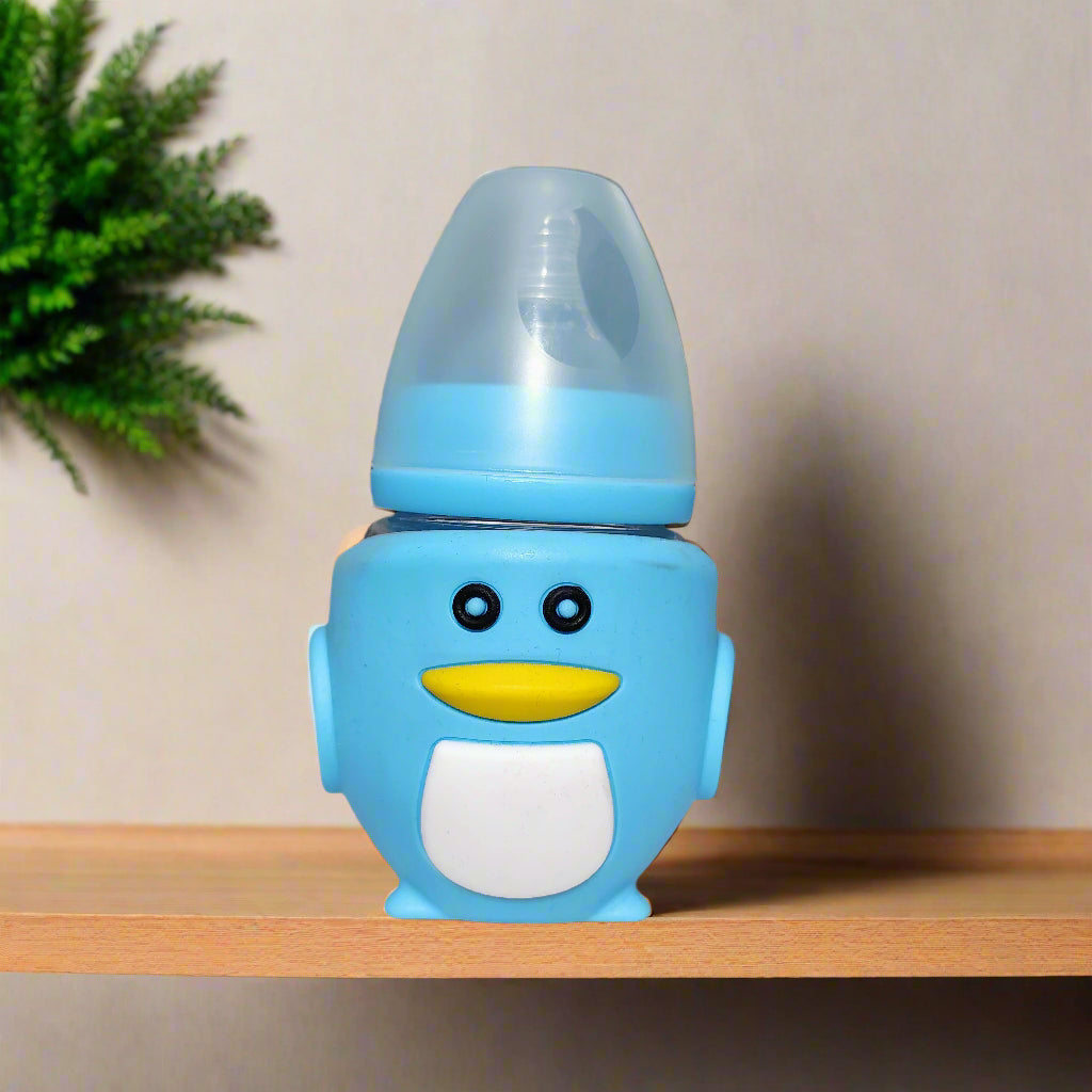 Blue penguin-shaped baby bottle on a white surface with a blurred indoor background