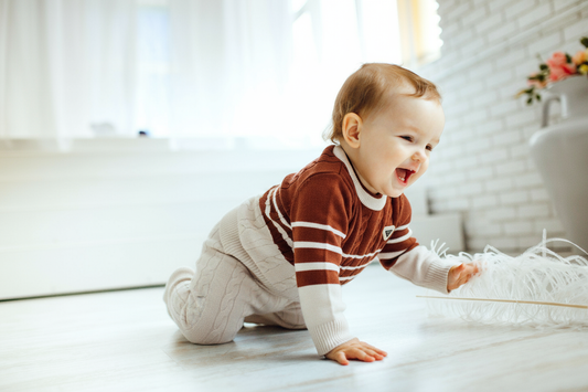 Baby in a striped sweater crawling on a light wooden floor.