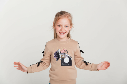 Young girl wearing a beige sweatshirt with a graphic design on a white background
