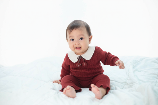 Baby in a red outfit sitting on a white blanket
