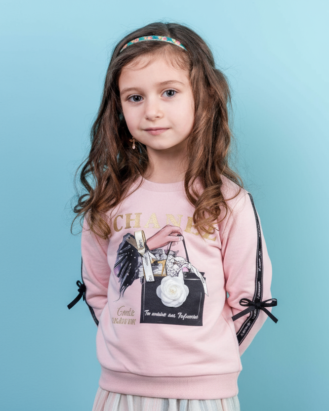 Young girl wearing a pink sweatshirt with decorative elements on a light blue background