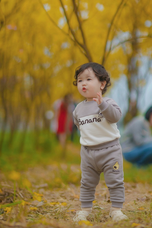 Child wearing a 'Banana' sweatshirt in an autumn setting with yellow leaves and blurred background